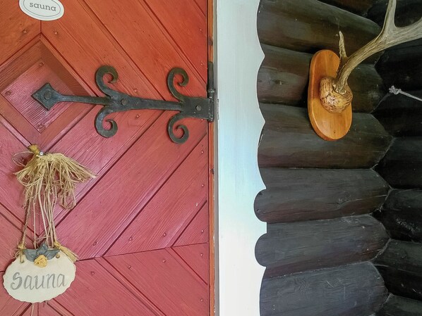 A red door with a metal handle and a sign reading 'Sauna'.