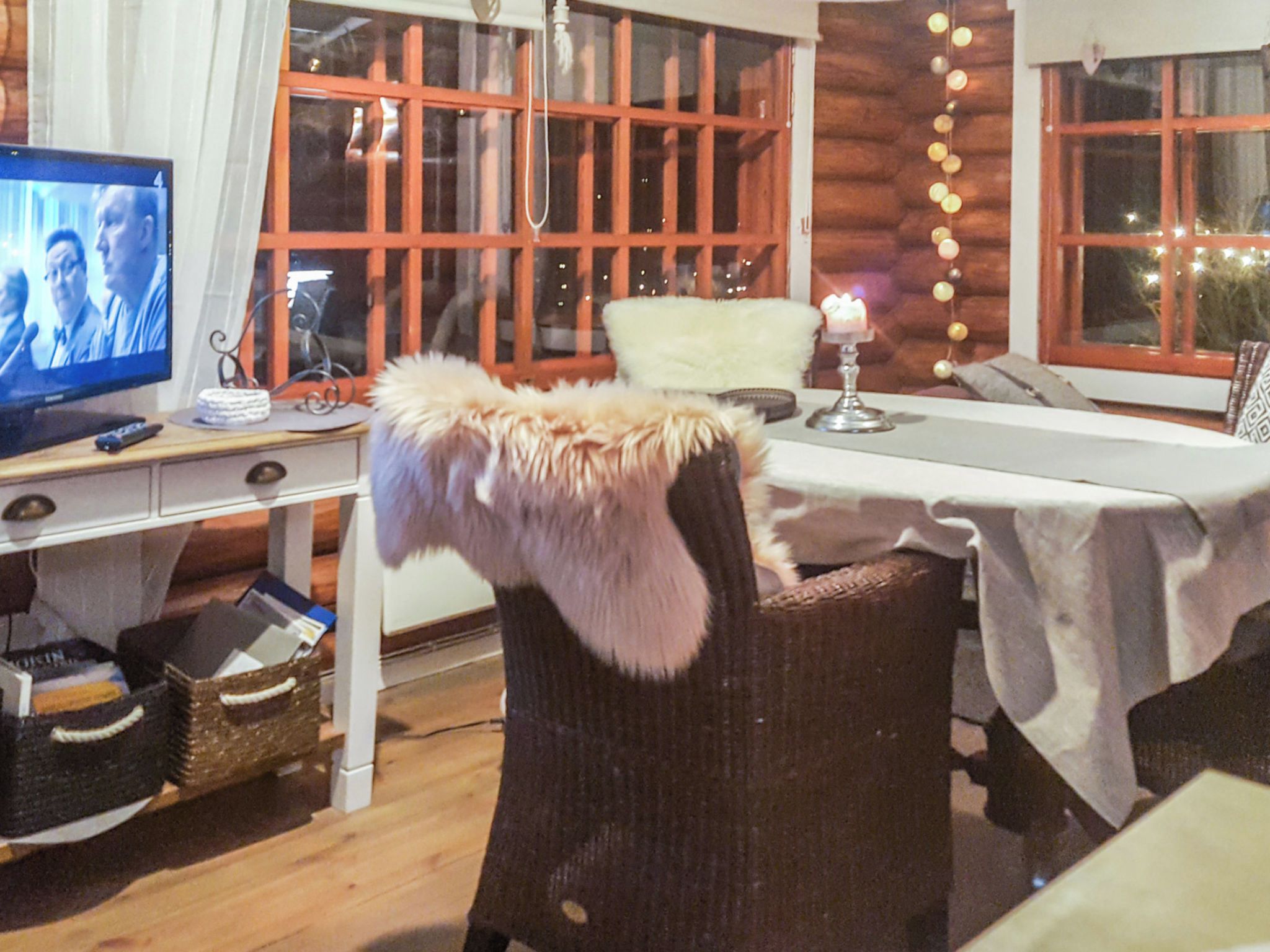 Ein gemütliches Zimmer mit Fernseher, Korbmöbeln und einem Tisch mit Kerze.