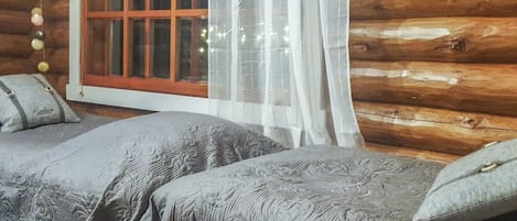 Een blokhutkamer met twee bedden, een raam met gordijnen en een decoratieve wand.