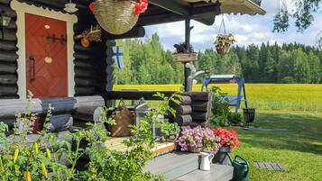 Eine Blockhütte mit Veranda, einer roten Tür und Blick auf ein grünes Feld.