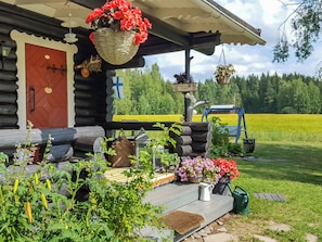 A log cabin with a porch, a red door, and a view of a green field.