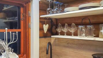 A kitchen with wooden cabinets, a window with a curtain, and various kitchenware including cups, plates, and jars.