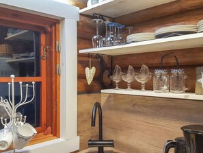 Une cuisine avec des meubles de rangement en bois, une fenêtre avec un rideau et divers ustensiles de cuisine, notamment des tasses, des assiettes et des bocaux.