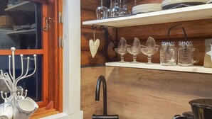 Cuina amb armaris de fusta, una finestra amb cortina i diferents utensilis de cuina, com ara tasses, plats i recipient de vidre.