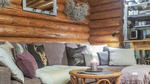 Interior acollidor d'una cabana de fusta, amb una paret de fusta, un sofà amb coixins i una taula de vimetlla petita amb una espelma, i una estantàlia amb recipients de cuina.