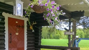 Una cabana de fusta amb una panxa de banc, una cistella de flors penjant i una porta amb un clavell.