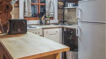 Eine Küche mit Holztisch, Herd, Geschirrspüler, Kühlschrank und einem Fenster mit Vorhängen.