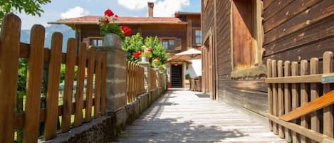 A wooden pathway leading to a building with a red roof, surrounded by a wooden fence and potted plants.