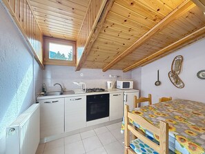 A compact kitchen with a window, a microwave, a sink, and a dining area with a table. - La Busa by Interhome (Alleghe)