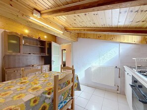 A rustic kitchen with wooden beams, a dining table with a sunflower tablecloth, and a white tiled floor. - La Busa by Interhome (Alleghe)