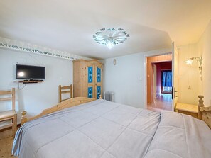 A bedroom with a bed, a television mounted on the wall, a wooden wardrobe, and a door leading to another room. - La Busa by Interhome (Alleghe)