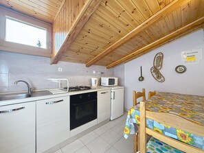 A compact kitchen with a stove, microwave, sink, and a dining area with a table. - La Busa by Interhome (Alleghe)