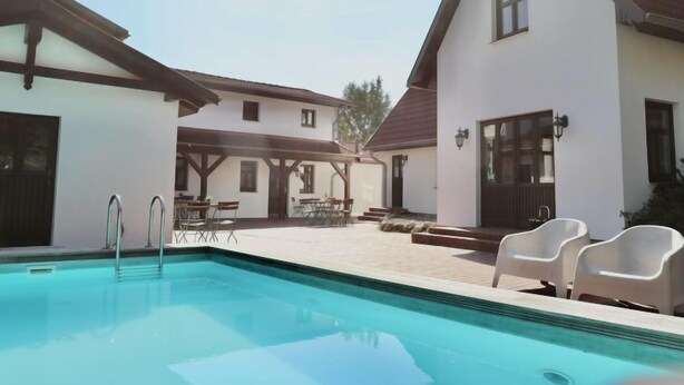 A swimming pool with a covered patio area, outdoor seating, and a building with a white facade and dark roof. - Hiddensee by Interhome (Dargun)