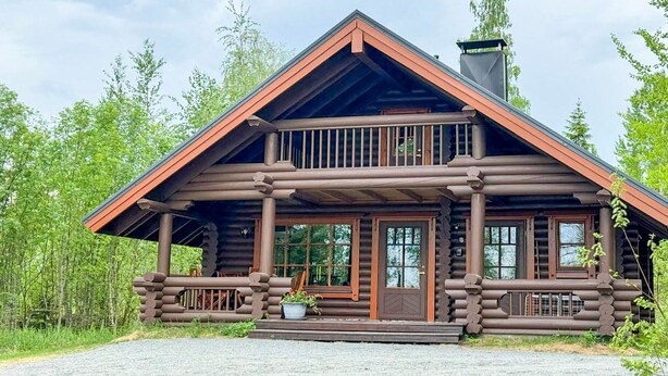 Eine Blockhütte mit Veranda, großen Fenstern und Schornstein.