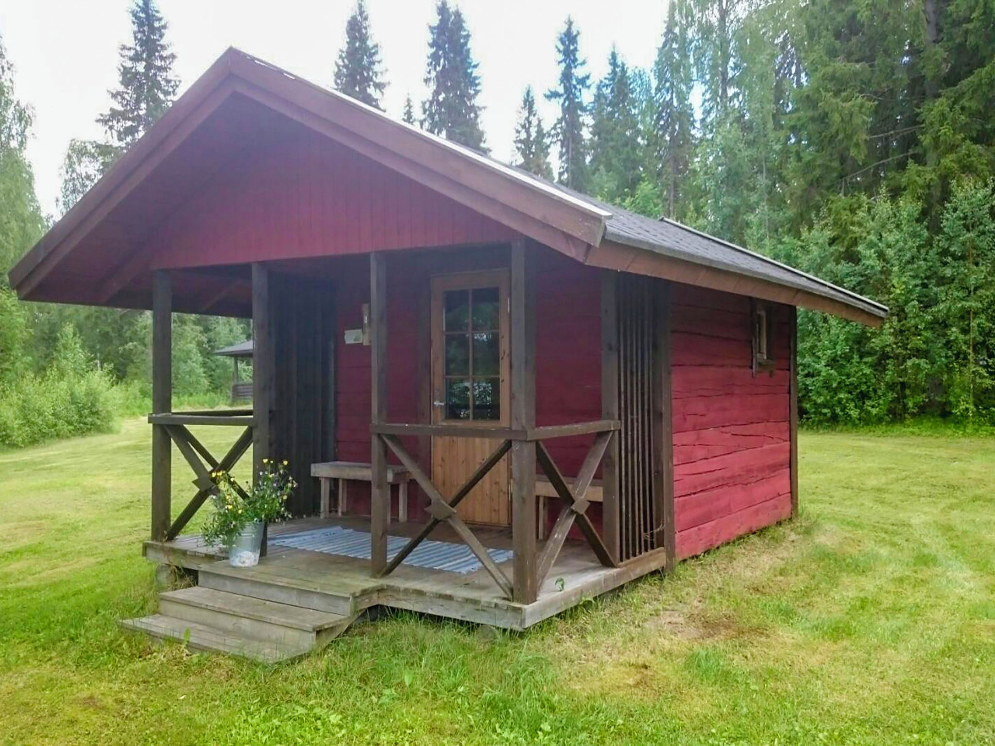 A small, single-story cabin with a porch, surrounded by a grassy area and trees.