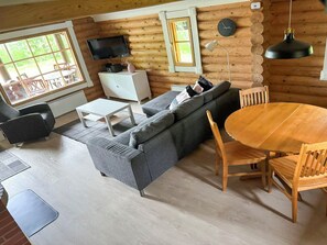 A log cabin interior with a sofa, dining table, chairs, a TV, and a clock on the wall.