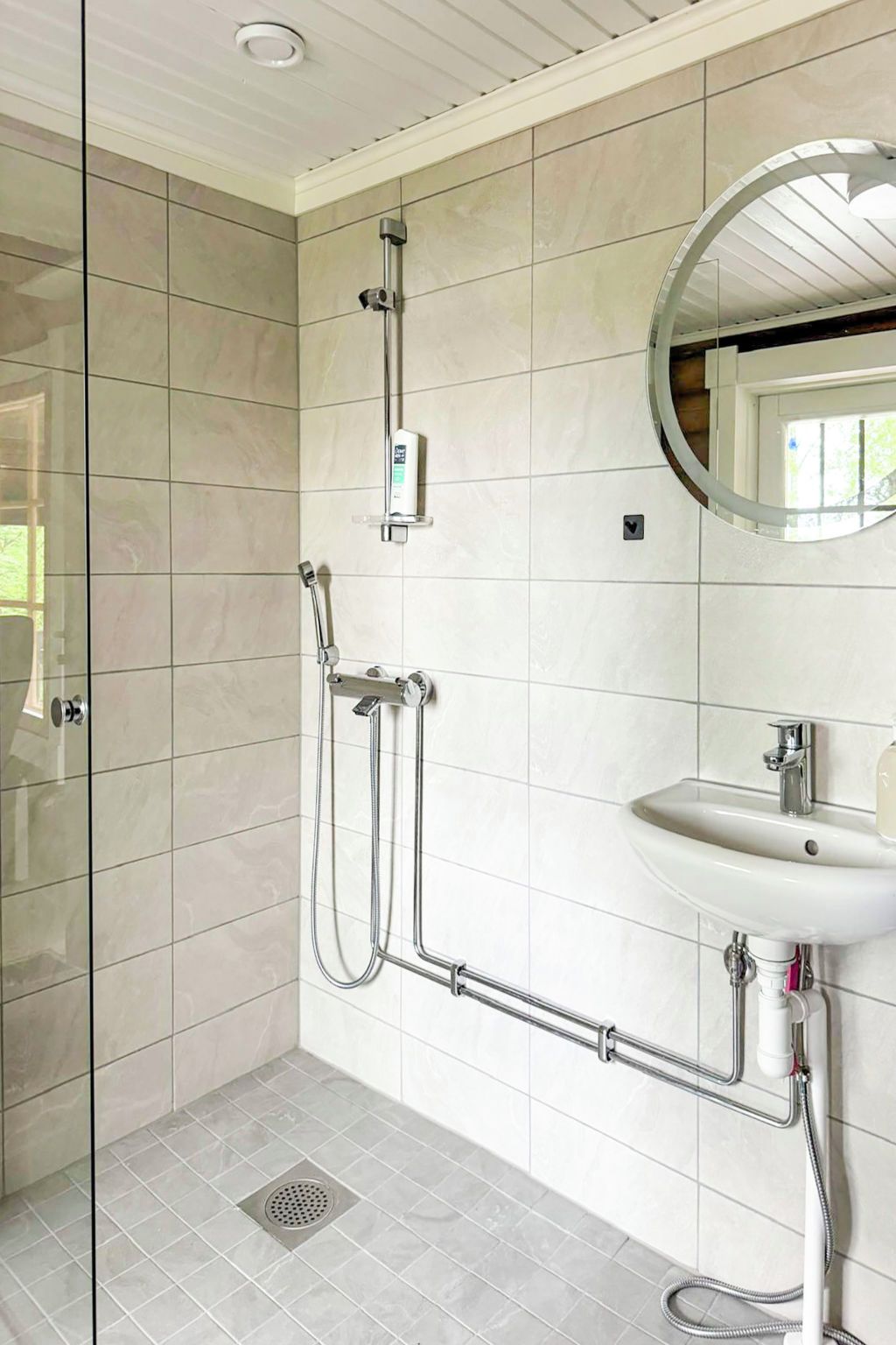 A modern bathroom with a glass shower enclosure, a wall-mounted sink, and a ceiling light.