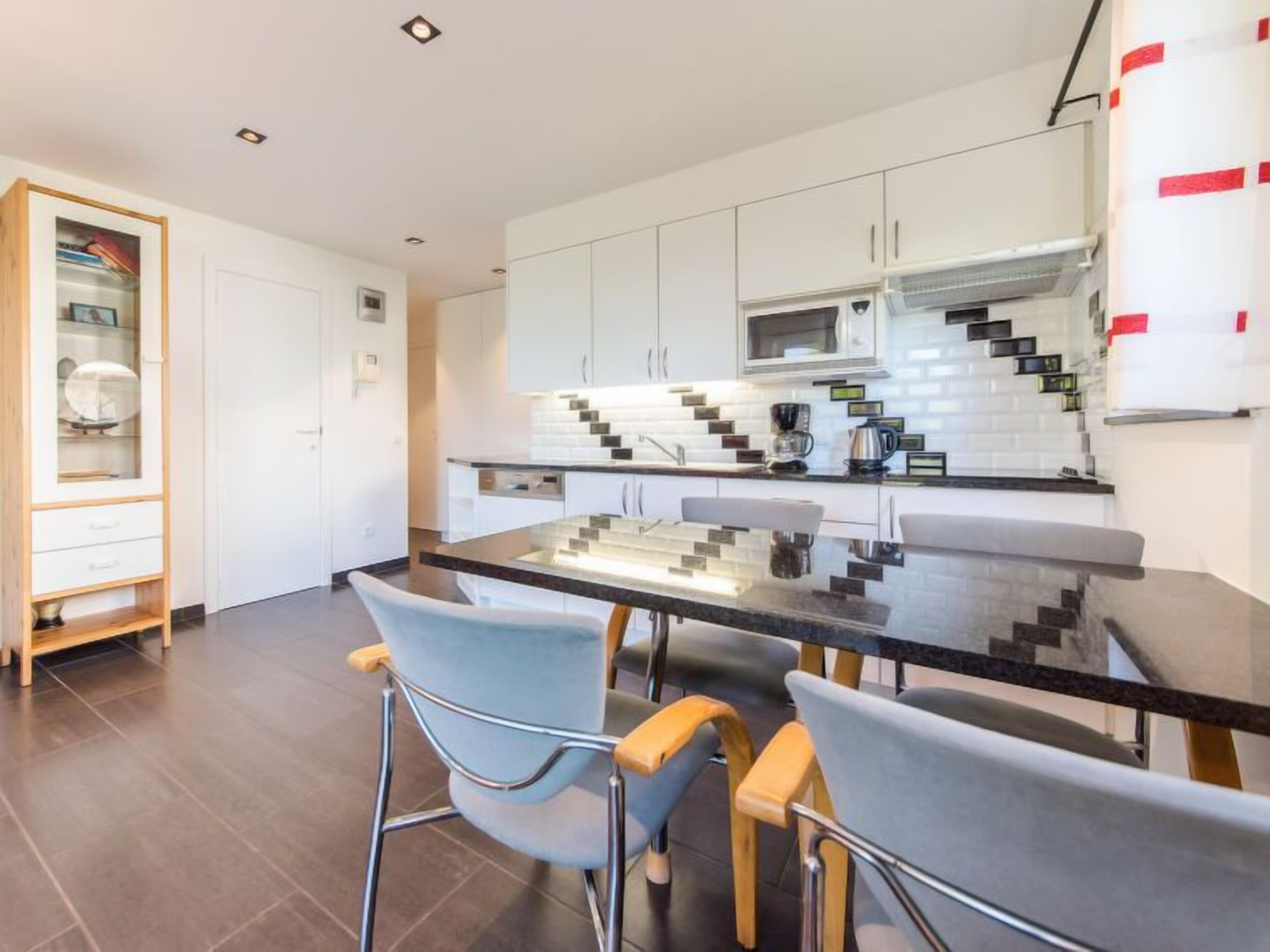 A modern kitchen with white cabinets, a black countertop, and a glass dining table.