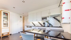 Une cuisine moderne avec des meubles blancs, un plan de travail noir et une table à manger en verre.