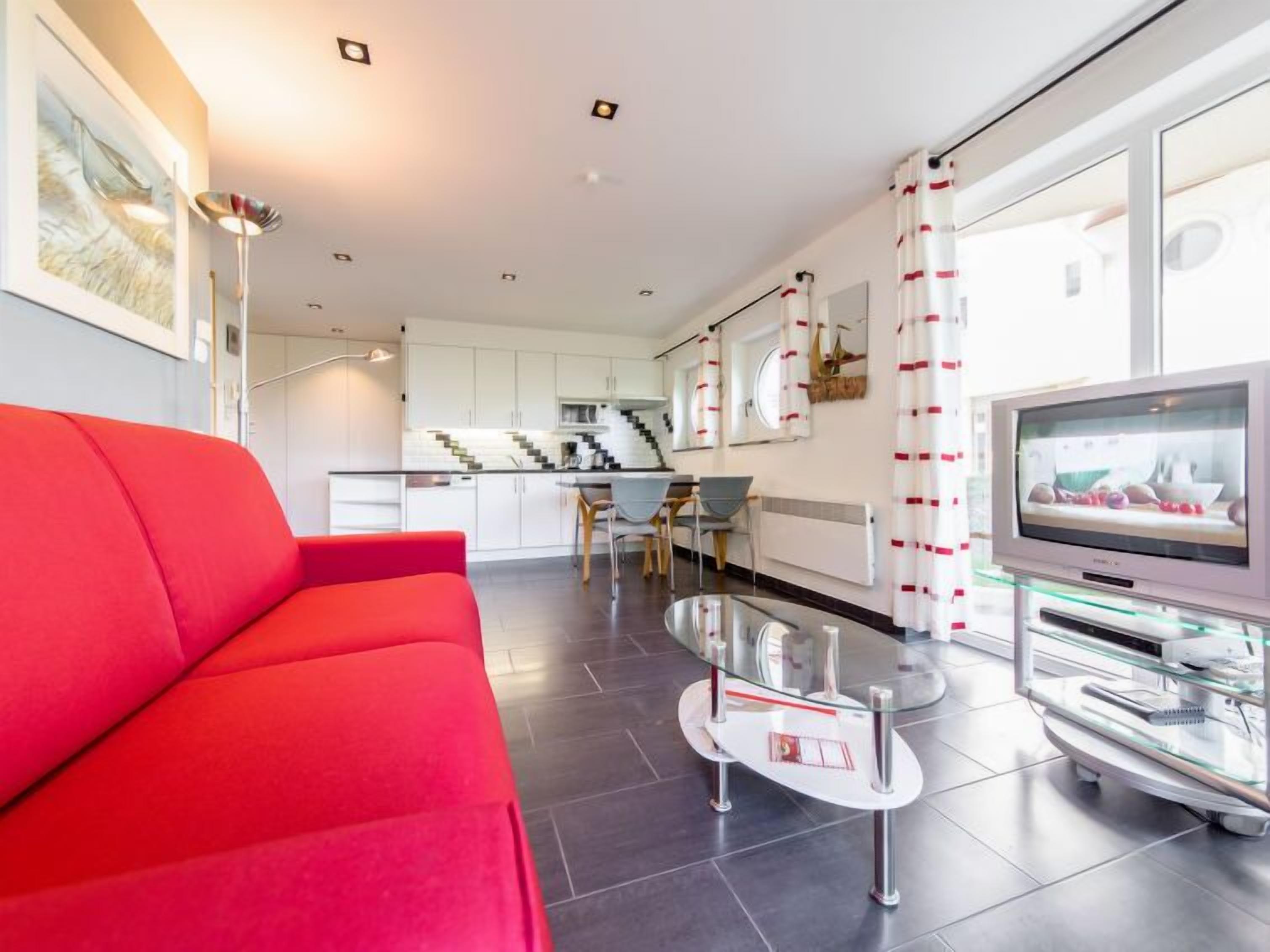 A modern living room with a red sofa, a glass coffee table, and a flat-screen TV.