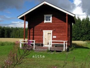 Situated in a serene grassy field, this cabin features a pitched roof and a small window above the door.