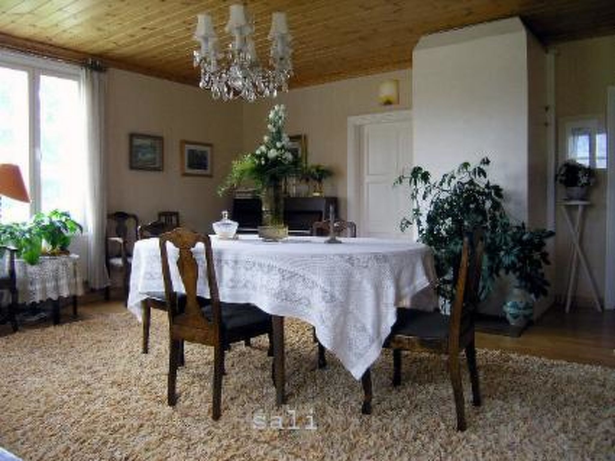 A dining area with a round table covered by a white tablecloth, surrounded by wooden chairs.