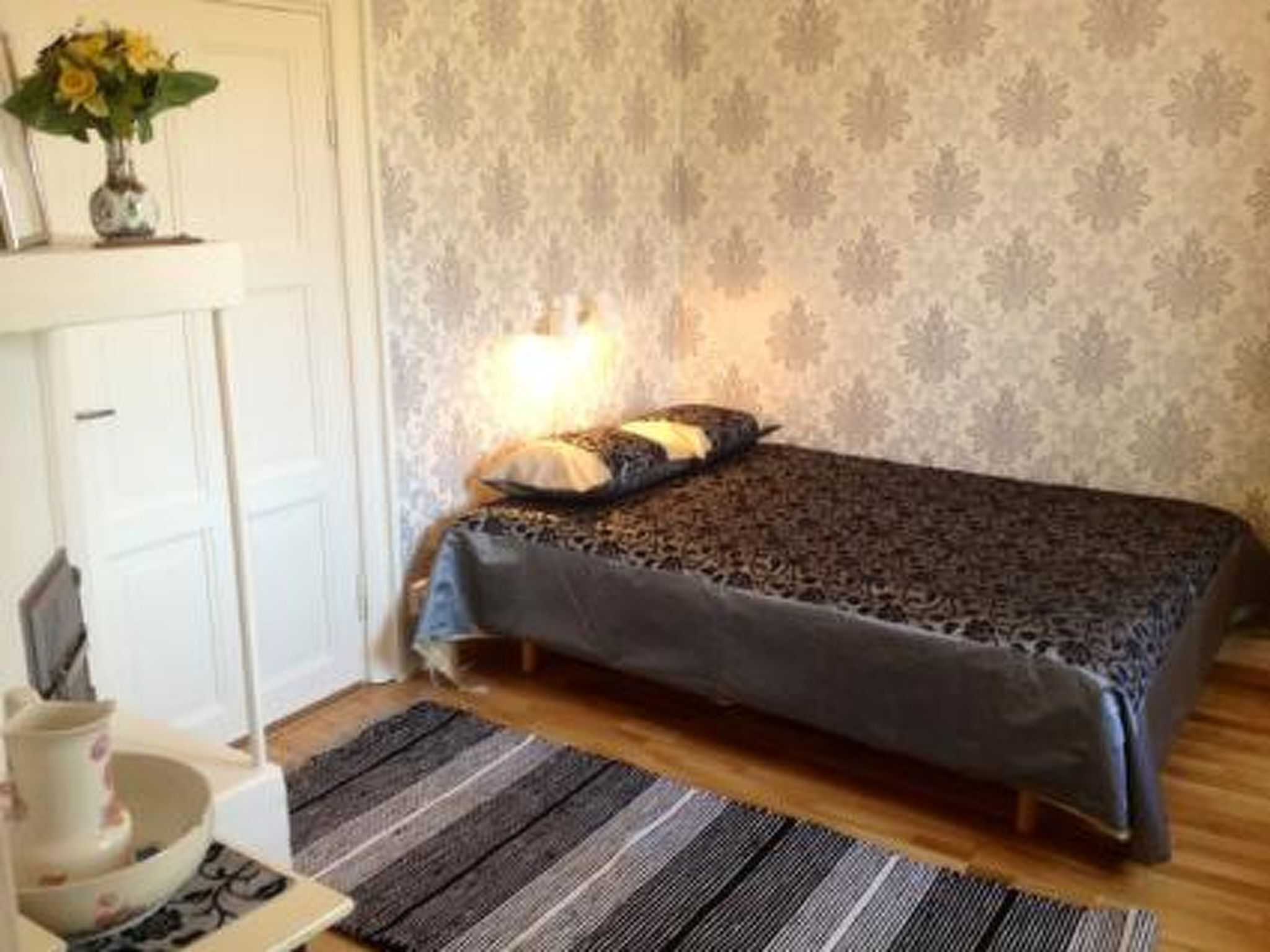 A bedroom with a bed, a nightstand, a lamp, and a patterned wallpaper.