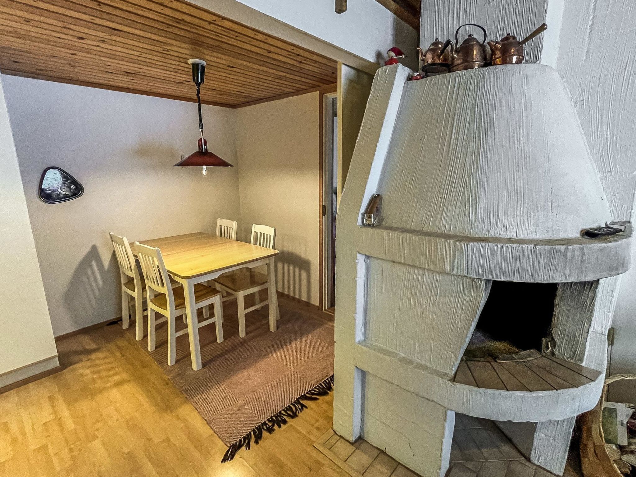 Ruokailutilassa on puinen pöytä ja tuolit, riippuvalaisin sekä kivinen takka, jossa on savupiippu.