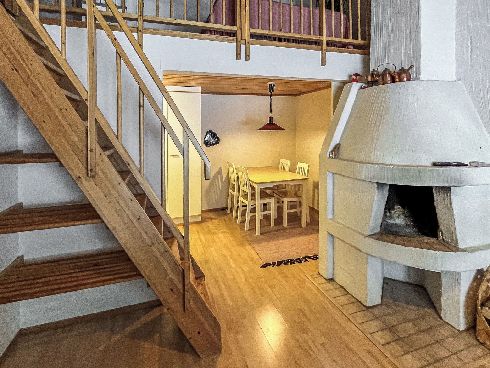 Eine Holztreppe führt zu einem Essbereich mit Tisch und Stühlen sowie einem Steinkamin.