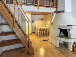 A wooden staircase leading to a dining area with a table and chairs, and a stone fireplace.