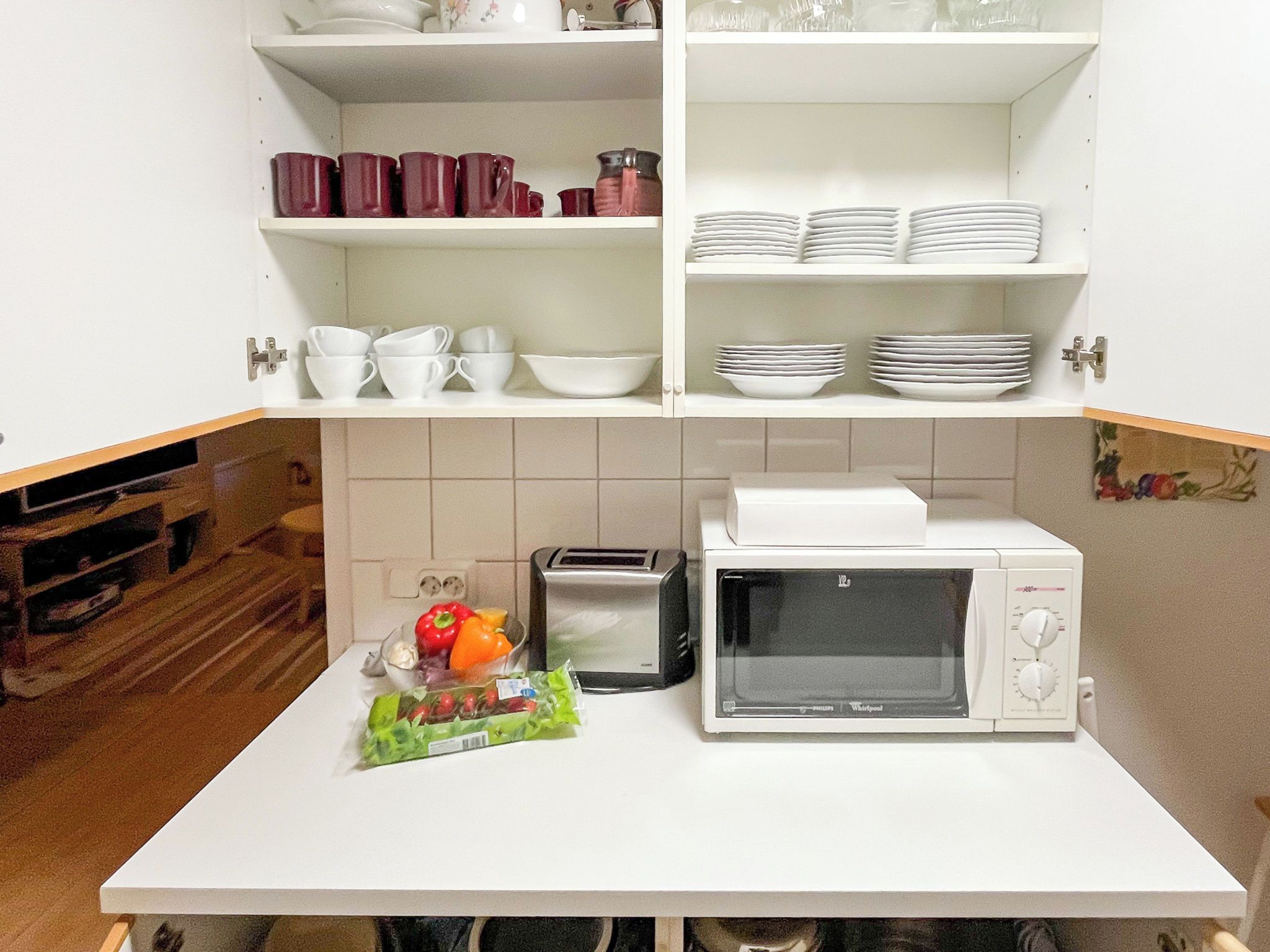 Une cuisine avec des meubles blancs, un four à micro-ondes, un grille-pain et un plan de travail sur lequel se trouve un sac de légumes.