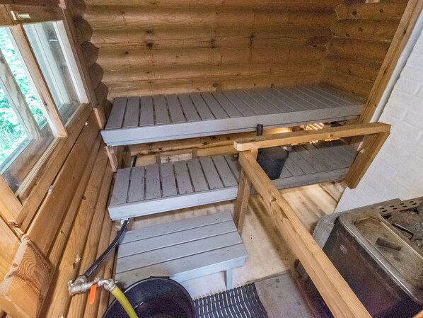 A wooden cabin interior with a metal stove, a window with a view of greenery, and a metal sink. - Koivurinne by Interhome (Punkaharju)