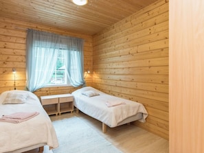 A small, cozy room with wooden walls and a window with curtains. There are two beds with pillows and a desk with a lamp. - Koivurinne by Interhome (Punkaharju)