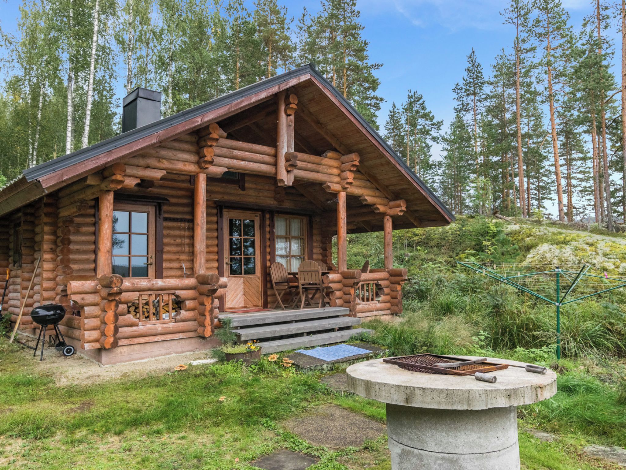 A log cabin with a porch, a grill, and a fire pit.
