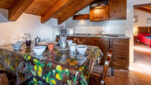 A cozy kitchen with wooden beams, a dining table with a fruit pattern tablecloth, and a microwave on the counter. - Grand Sarriod by Interhome (St Nicolas)