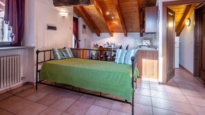 A room with a bed, a radiator, a window with curtains, and a kitchen area. - Grand Sarriod by Interhome (St Nicolas)