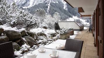 Ein mit Schnee bedeckter Außenbereich mit Blick auf die Berge, mit einem Tisch, einer Teekanne und Tassen, sowie Zimmerpflanzen.