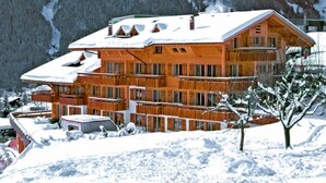 Una cabaña de madera de varios pisos con balcones, rodeada de montañas nevadas.