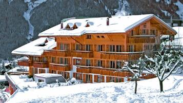 Ein mehrstöckiges Holzchalet mit Balkonen, umgeben von schneebedeckten Bergen.
