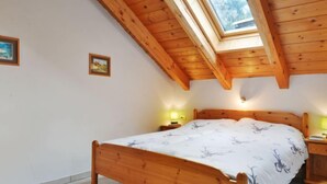 Quarto com cama de madeira, claraboia e duas luminárias de cabeceira.