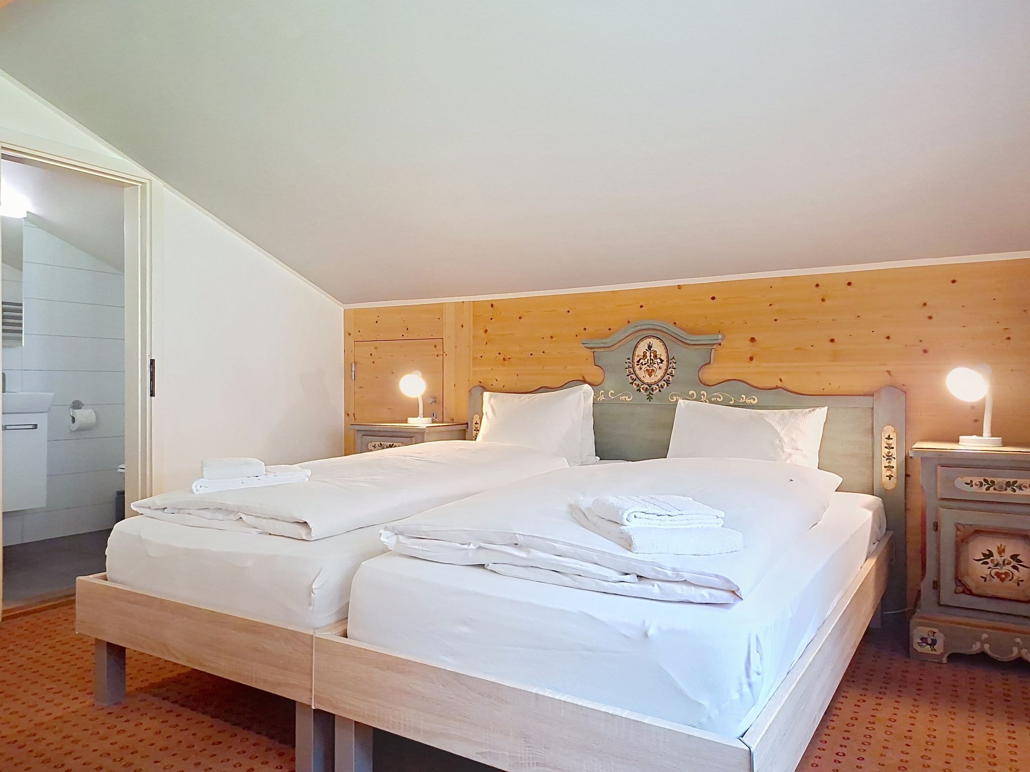 A double bed with white linens, a wooden headboard, bedside lamps, and a wooden nightstand with a decorative item.