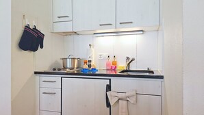 A compact kitchen with white cabinets, a black countertop, a pot on the stove, and various kitchen items. - Chalet Schwendihus by Interhome (Grindelwald)