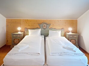 Ein Doppelbett mit weißen Leinentüchern, zwei Nachttische mit Lampen und ein Holzkopfteil mit dekorativen Schnitzereien.