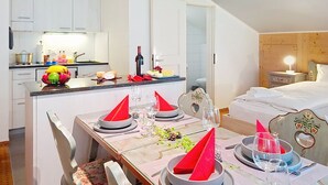 A dining area with a table set for four, a kitchen in the background, and a bedroom with a bed and nightstand. - Chalet Schwendihus by Interhome (Grindelwald)