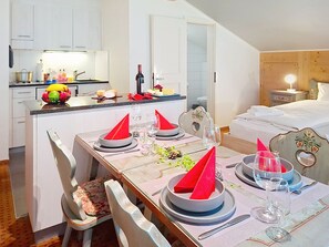 Un coin repas avec une table dressée pour quatre personnes, une cuisine en arrière-plan et une chambre à coucher avec un lit et une table de chevet.