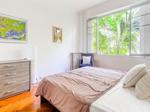 A bedroom with a bed, a dresser, a chair, a window with a view of greenery, and a map on the wall.