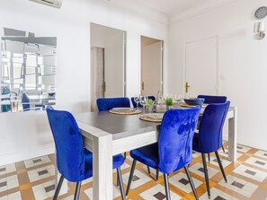A dining area with a rectangular table, blue velvet chairs, and a modern mirror on the wall.