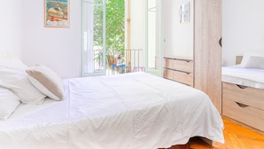 Ein Schlafzimmer mit einem Bett, einem Holzschrank, einem kleinen Tisch mit einer Vase und einem Balkon mit Blick ins Grüne.