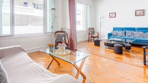 Ein modernes Wohnzimmer mit einem Glastisch, einem blauen Sofa und Holzboden.