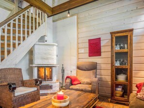 A cozy interior with a fireplace, a wooden staircase, a wicker chair, a cushioned sofa, and a wooden cabinet with glass doors.